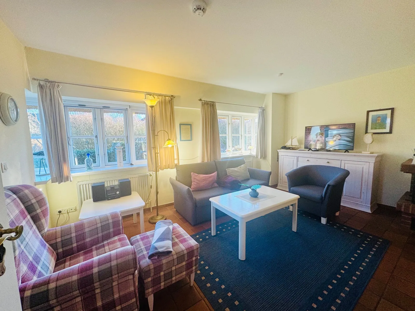 Wohnzimmer mit Sofa, karierten Sesseln und TV in der Ferienwohnung auf Föhr