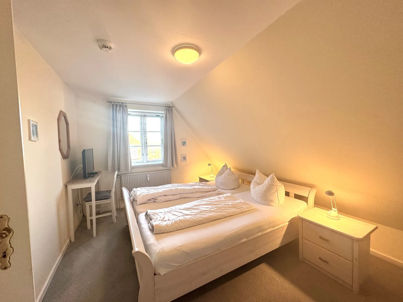 Doppelbett mit Nachttischen am Fenster im Schlafzimmer unter dem Reetdach